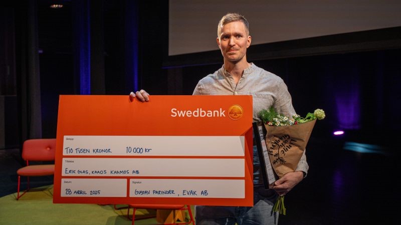 Halvkroppsporträtt inomhus av Erik Glas. Han håller upp en stor check och en blombukett