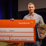 Halvkroppsporträtt inomhus av Erik Glas. Han håller upp en stor check och en blombukett