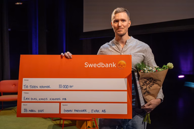 Halvkroppsporträtt inomhus av Erik Glas. Han håller upp en stor check och en blombukett