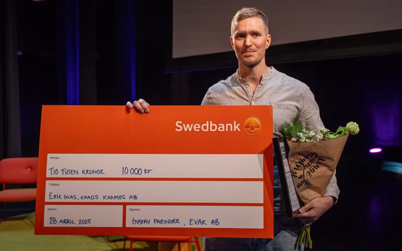 Halvkroppsporträtt inomhus av Erik Glas. Han håller upp en stor check och en blombukett
